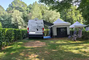 Wohnmobil mit Markise und Vorzelt auf dem Campingplatz, daneben Klappstühle und Zeltplanen im Grünen.