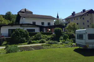 Campingplatz-Gebäude mit gepflegtem Garten und Wohnwagen am Rand, Hecken und Rasen vor den Häusern.