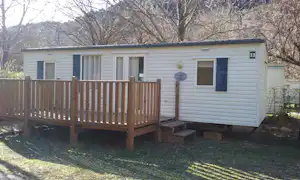 Weiße Wohnwagen-Unterkunft mit Holzveranda und Stufen, Nummer 33, im Grünen vor Bäumen und Hecke.