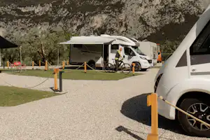 Wohnmobil auf einem Stellplatz mit Kiesfläche, Holzpfosten und Blick auf einen felsigen Berg im Hintergrund.