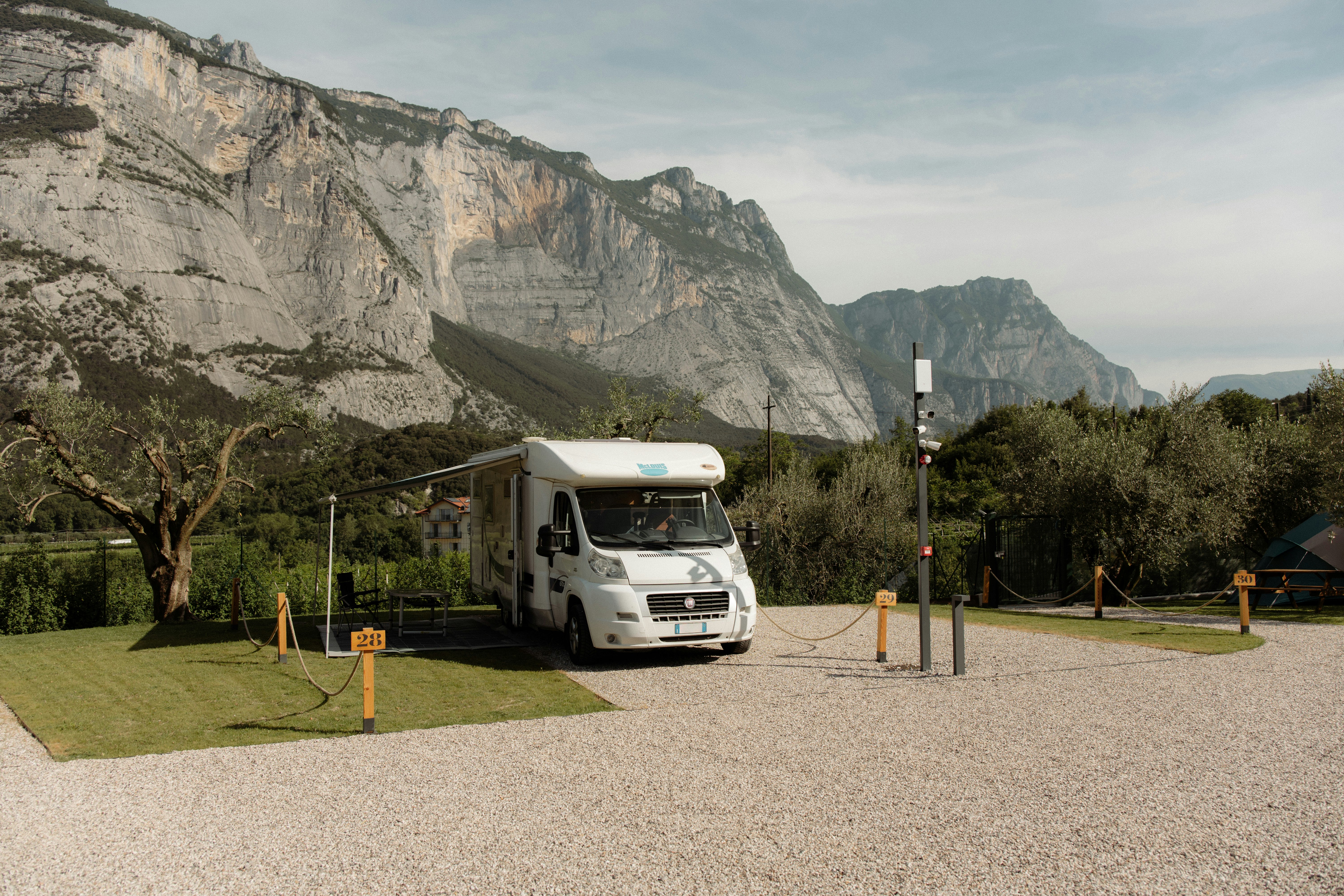 Wohnmobil auf einem Kiesstellplatz, im Hintergrund Berge und Felsen, daneben Bäume und ein Stromanschluss.