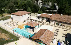 Blick auf einen Campingbereich mit Pool, Liegen und Terrassen an mehreren Gebäuden, umgeben von Bäumen und Felswand.