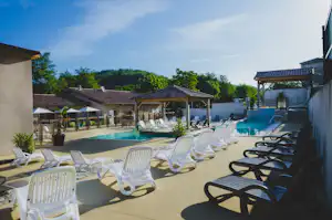 Poolbereich mit mehreren Sonnenliegen am Campingplatz, im Hintergrund Gebäude und Bäume.