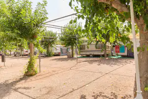 Wohnmobile auf dem Campingplatz, durch Bäume und ein Metallgestell mit Planen überspannt, im Hintergrund weitere Fahrzeuge.