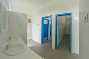 Camping-Badezimmer mit zwei blauen Türen, weißen Fliesen, Waschbecken und Spiegeln an den Wänden.