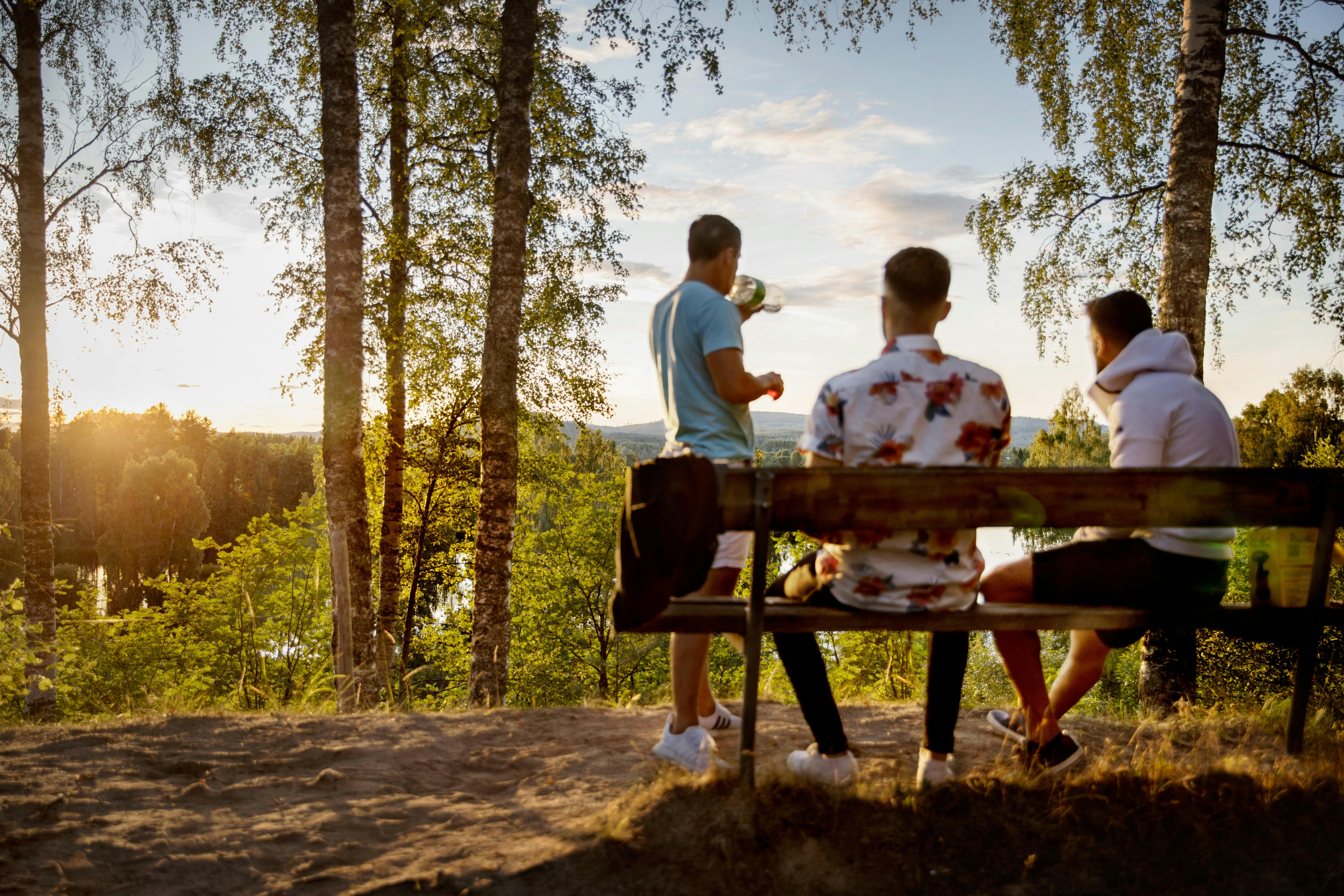 Familie am Camping-Tisch im Wald, Erwachsene und Kinder sitzen und schauen in die Ferne bei goldenem Sonnenlicht.