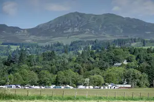 Campingplatz mit Wohnwagen und Zelten am Rand einer Wiese, Blick ins Tal mit Wald und hohen Bergen.