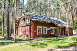 Rotes Ferienhaus im Wald mit Satteldach, Terrasse und Blumen vor den Fenstern, daneben Fahrräder am Weg.