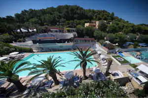 Blick auf den Camping-Pool mit Palmen, Liegestühlen und Sonnenschirmen, im Hintergrund Gebäude und Bäume.