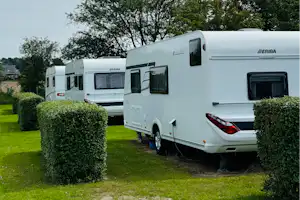 Wohnwagen auf einem Campingplatz, mit Hecken und Rasenfläche, im Hintergrund weitere Wohnwagen und Bäume.