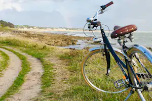 Fahrrad am Küstenweg, Blick auf das Meer mit Felsen und Sträuchern entlang der Promenade.