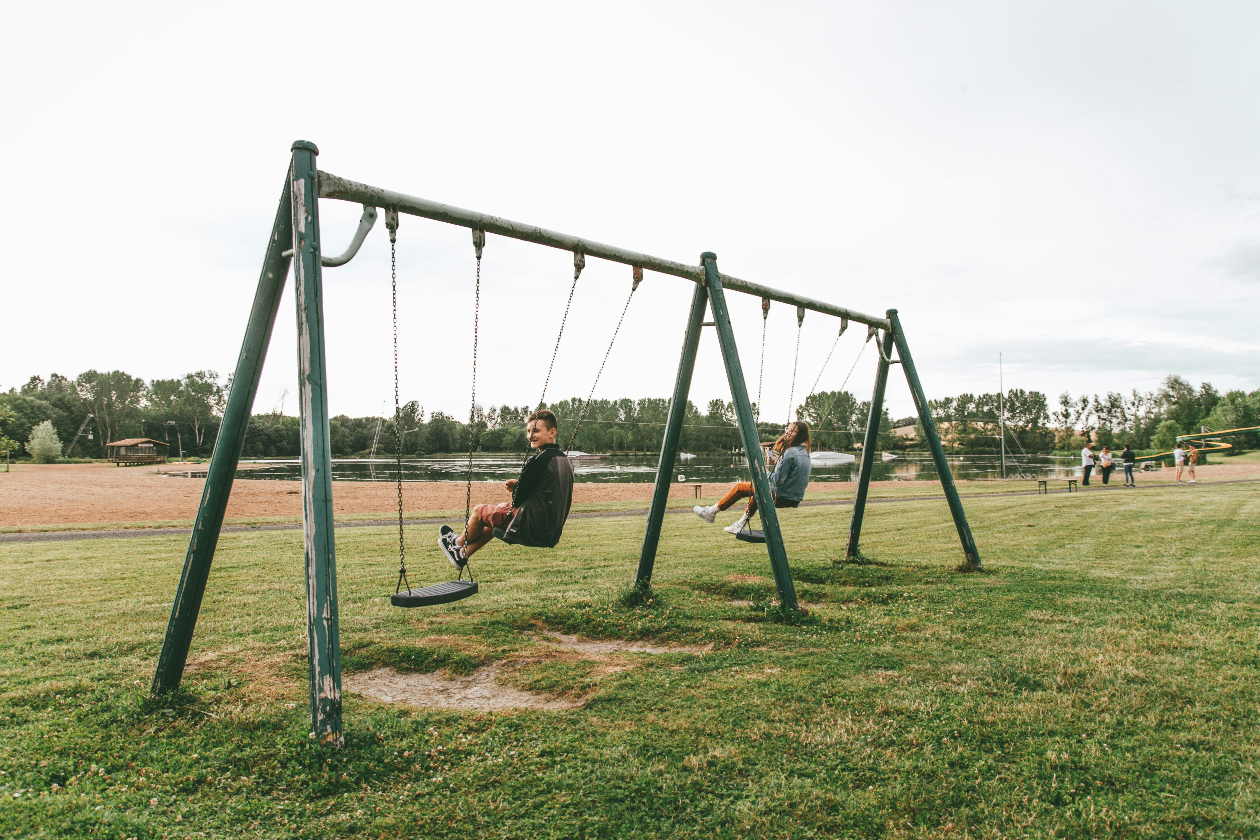 Schaukeln auf einem Spielplatz im Campingbereich, mit Rasenfläche und Bäumen im Hintergrund.
