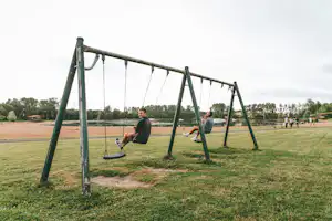 Schaukeln auf einem Spielplatz im Campingbereich, mit Rasenfläche und Bäumen im Hintergrund.