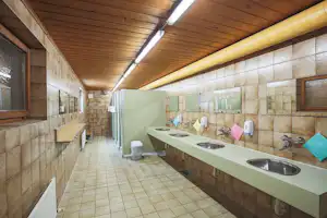 Camping Montafon - Innenraum des Sanitärgebäudes mit Waschbecken und Toilettenkabinen im Hintergrund