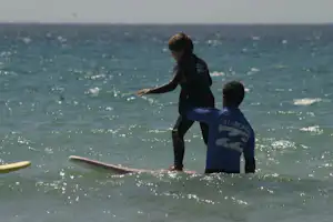 Zwei Kinder auf einem Surfbrett im Meer, im Hintergrund die weite Wasserfläche und Sonnenreflexe.