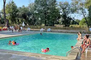 Camping-Pool mit mehreren Kindern und Erwachsenen im Wasser, Liegen am Beckenrand und Zaun mit Bäumen im Hintergrund.