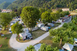 Luftaufnahme eines Campingplatzes mit Wohnwagen und Zelten, gepflasterten Wegen, Bäumen und einem Gebäude am Rand.