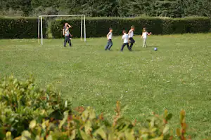 Kinder spielen Fußball auf einer Wiese vor einem Tor, im Hintergrund Hecken und Bäume auf dem Campingplatz.
