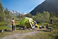 Camping Morteratsch - Sitzender Camper vor dem Zelt auf der Wiese der Campingplatzanlage mit Blick auf die Berge