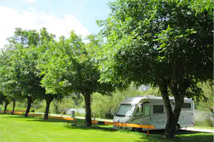 Wohnmobil auf einem Stellplatz im Grünen, mit Holzbegrenzung und Bäumen im Vordergrund.