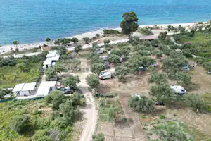 Campingplatz an der Küste mit Stellplätzen, Wegen und Wohnmobilen nahe dem Meer, umgeben von Bäumen und Grünflächen.