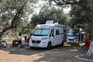 Wohnmobil auf dem Stellplatz zwischen Olivenbäumen, mit Vorzelt, Tisch und Stühlen sowie weiteren Campern im Hintergrund.