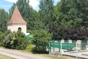 Kleine Kapelle am Campingplatz, umgeben von Bäumen, daneben ein eingezäunter Bereich mit Sitzgelegenheiten.