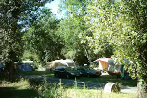 Campingplatz im Grünen: Wohnmobile und Zelte zwischen Bäumen, mit Autos auf dem Stellplatz.