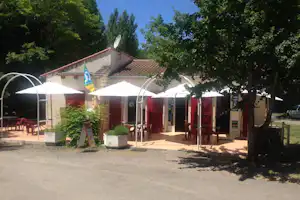 Terrasse am Campingplatz mit weißen Sonnenschirmen, roten Stühlen und Tischen vor einem Gebäude, umgeben von Bäumen.