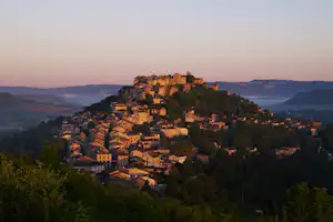 Italienisches Bergdorf mit vielen Häusern auf einem Hügel, umgeben von Tälern und bewaldeten Hängen bei Dämmerung.