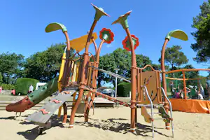Spielplatz-Klettergerüst mit Rutsche und Kletterelementen auf dem Campingplatz, Sandboden und Bäume im Hintergrund.