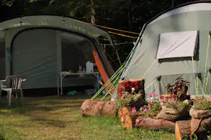 Zwei Campingzelte mit Vorzelt, Campingstühlen und Tisch auf dem Rasen, im Hintergrund Bäume und Blumenbeete.