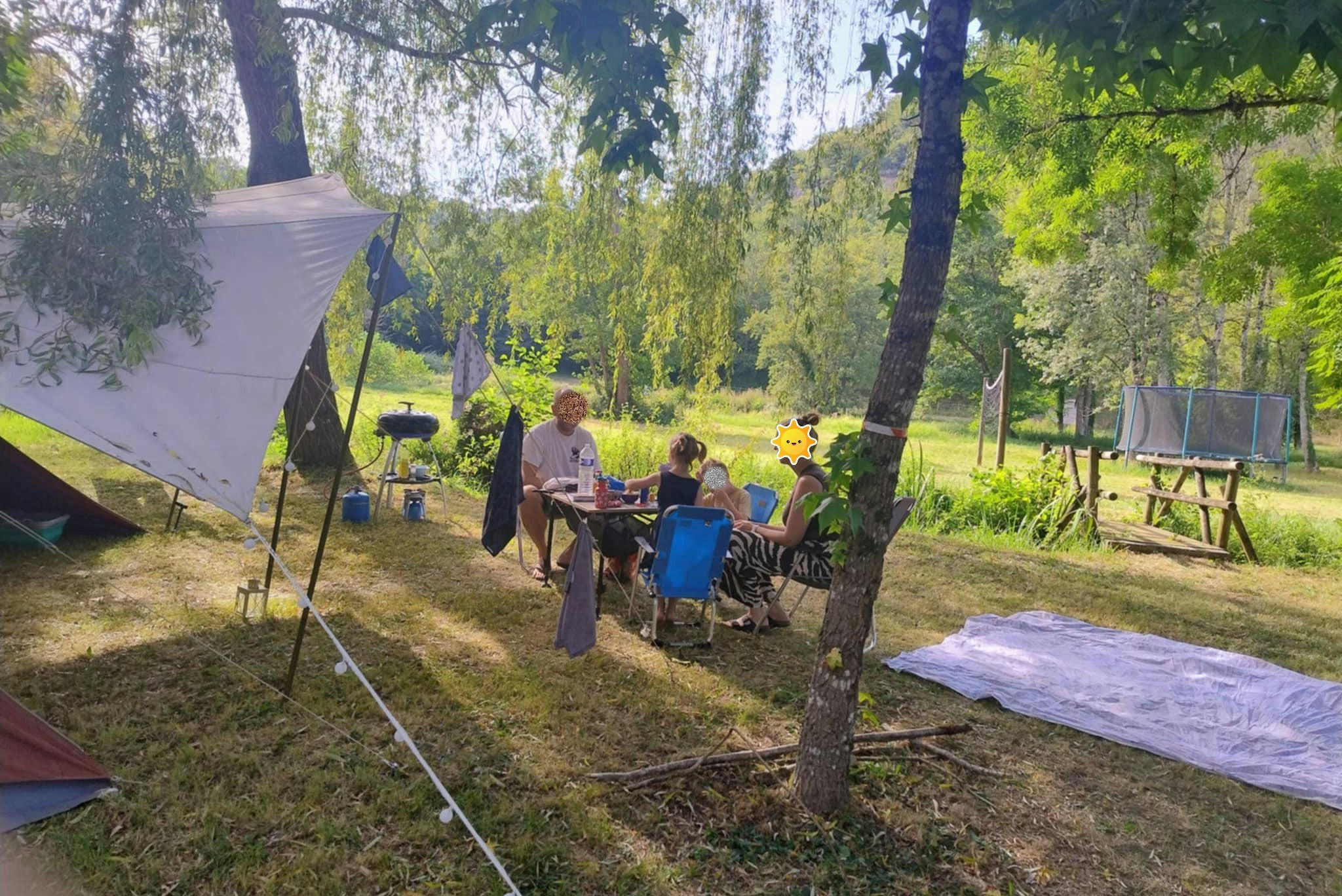 Campingplatz mit Zelt, Tisch und Stühlen im Grünen, daneben weitere Campingausrüstung zwischen Bäumen.