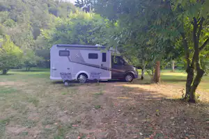 Wohnmobil auf einem Campingplatz-Stellplatz im Grünen, mit Vorzelt und Tisch am Boden, umgeben von Bäumen und Wiese.