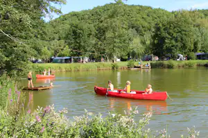 Rote Ruderboote auf einem See, im Hintergrund Campingzelte und Bäume am Ufer.