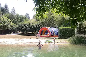 Zelt am Seeufer im Grünen, im Hintergrund weitere Zelte und Bäume, im Wasser schwimmen Personen.