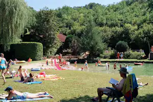 Badebereich am Campingplatz mit Schwimmbecken im See, Liegen, Luftmatratzen und Rutsche vor dichtem Grün.