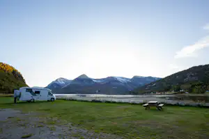 Wohnmobil auf einem Campingplatz auf einer Wiese, im Hintergrund Berge und ein See.