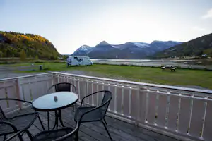 Balkon mit Tisch und Stühlen, davor ein Wohnmobil auf dem Campingplatz, im Hintergrund Berge und grünes Tal.