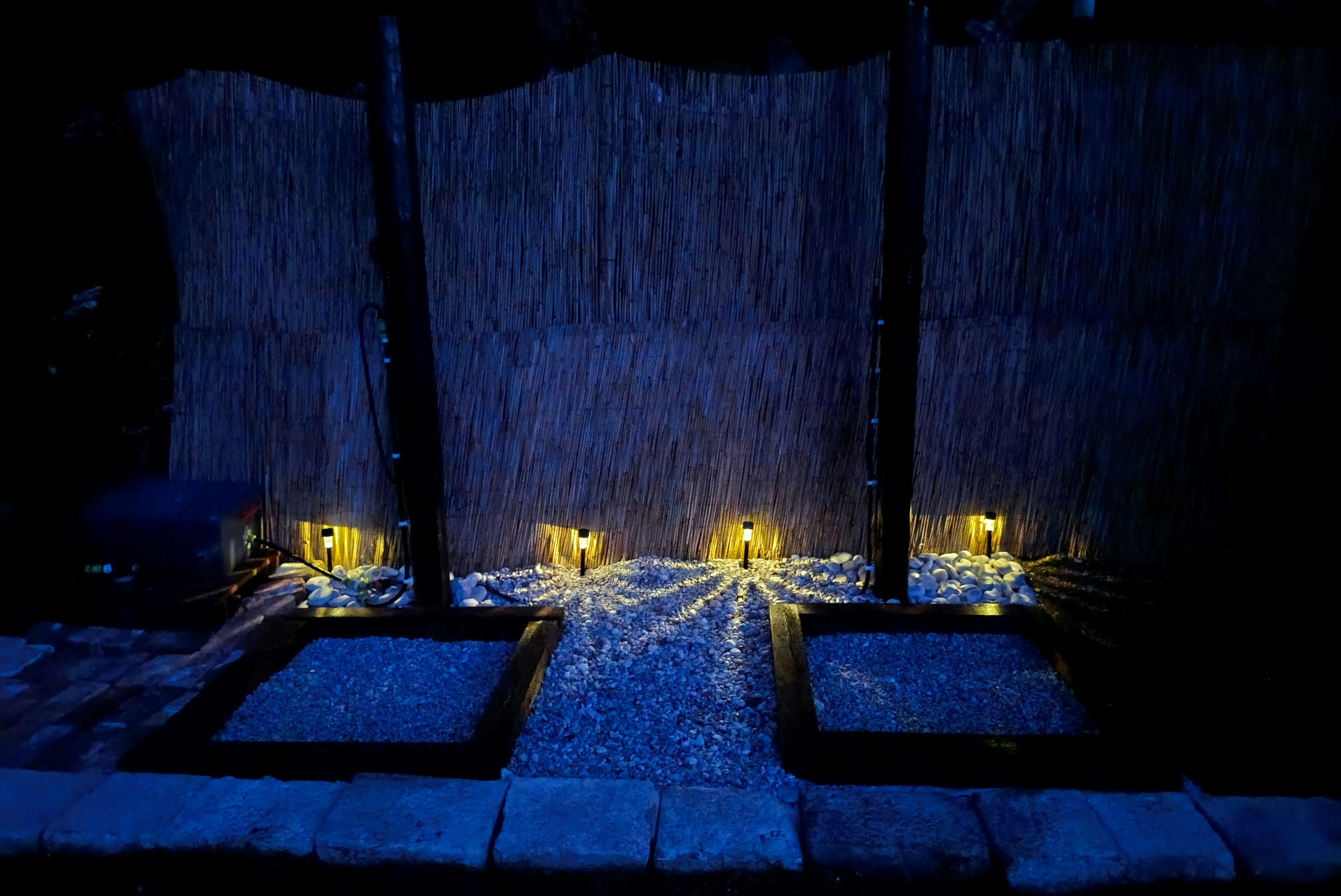 Beleuchtete Steinwege und kleine Terrassen am Campingplatz bei Nacht, mit Sichtschutzzaun und Laternen entlang der Wege.
