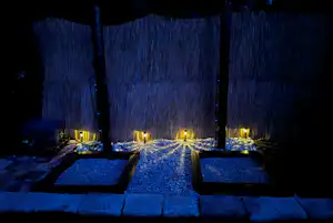 Beleuchtete Steinwege und kleine Terrassen am Campingplatz bei Nacht, mit Sichtschutzzaun und Laternen entlang der Wege.