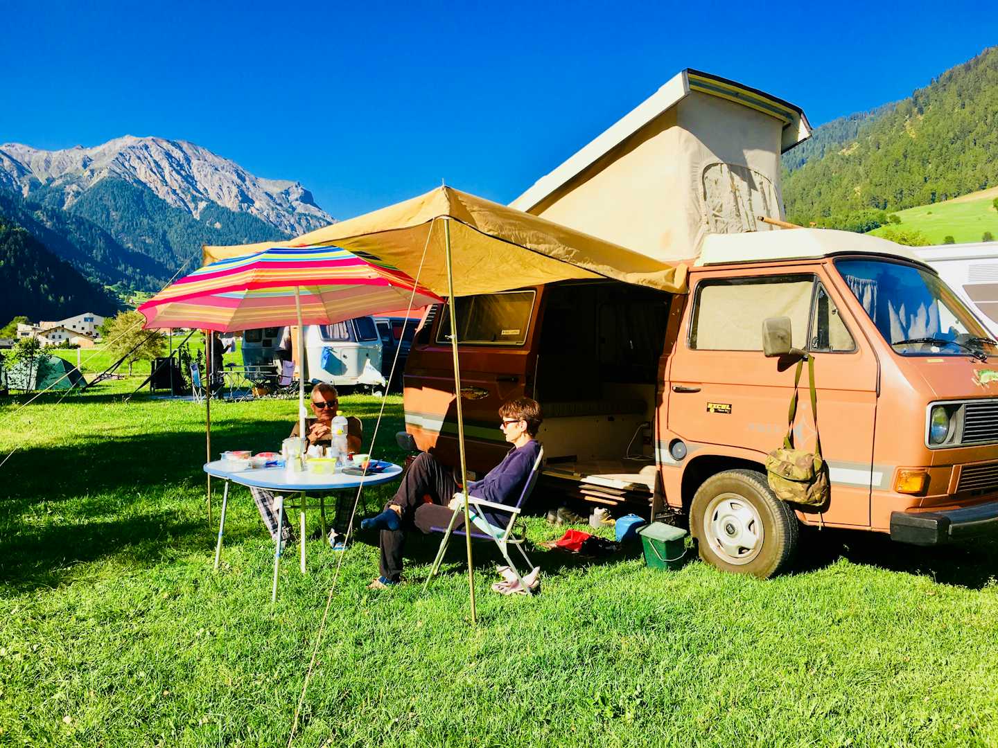 Camping Muglin - Camper sitzen vor dem Wohnmobil im Schatten der Markise 