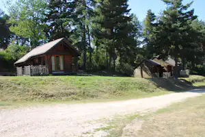 Holzhütten auf einem Campingplatz im Grünen, mit Veranda, Holzgeländer und Wegen zwischen den Bäumen.