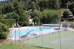 Schwimmbecken mit Liegen am Campingplatz, im Vordergrund ein Sportplatzzaun und Bäume im Hintergrund.