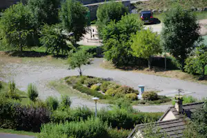 Campingplatz mit Baumreihen, gepflasterten Stellplätzen und einem Auto am Rand der Wiese.