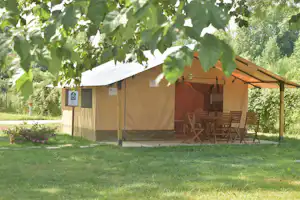 Zelt mit Holzstühlen und Tisch auf einem grünen Rasen, umgeben von Bäumen und Hecken im Campingbereich.