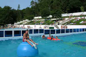 Schwimmbecken auf dem Campingplatz mit Badegästen, Kindern auf Schwimmreifen und einem großen Rutschbereich im Hintergrund.