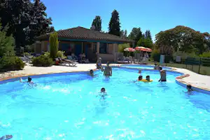 Camping-Pool mit mehreren Personen im Wasser, Liegen am Rand und ein Gebäude mit Terrasse im Hintergrund.