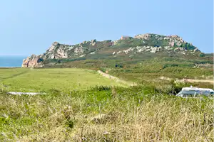 Blick auf die Küste mit Meer und grünen Hügeln, im Vordergrund Gras und ein Wohnmobil am Weg.