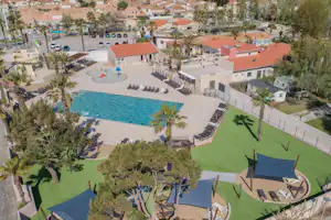 Luftaufnahme vom Campingplatz mit großem Pool, Sonnenschirmen, Liegen, Spielbereich und roten Dächern der Unterkünfte.